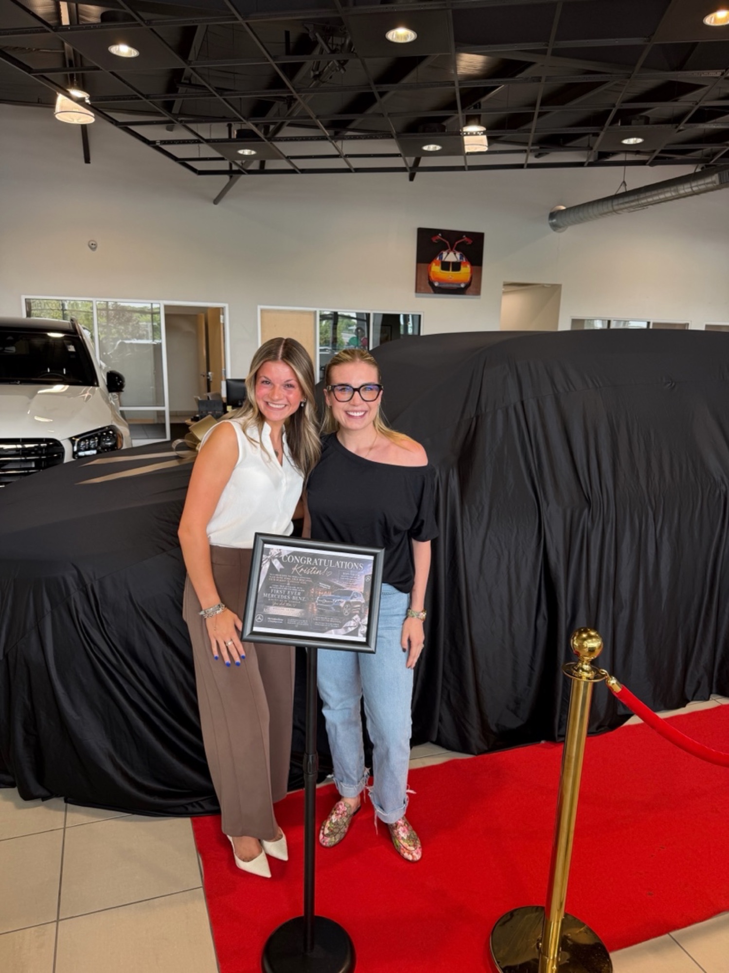 Kristin and Fiona beside the sign, on the red carpet at the dealership.